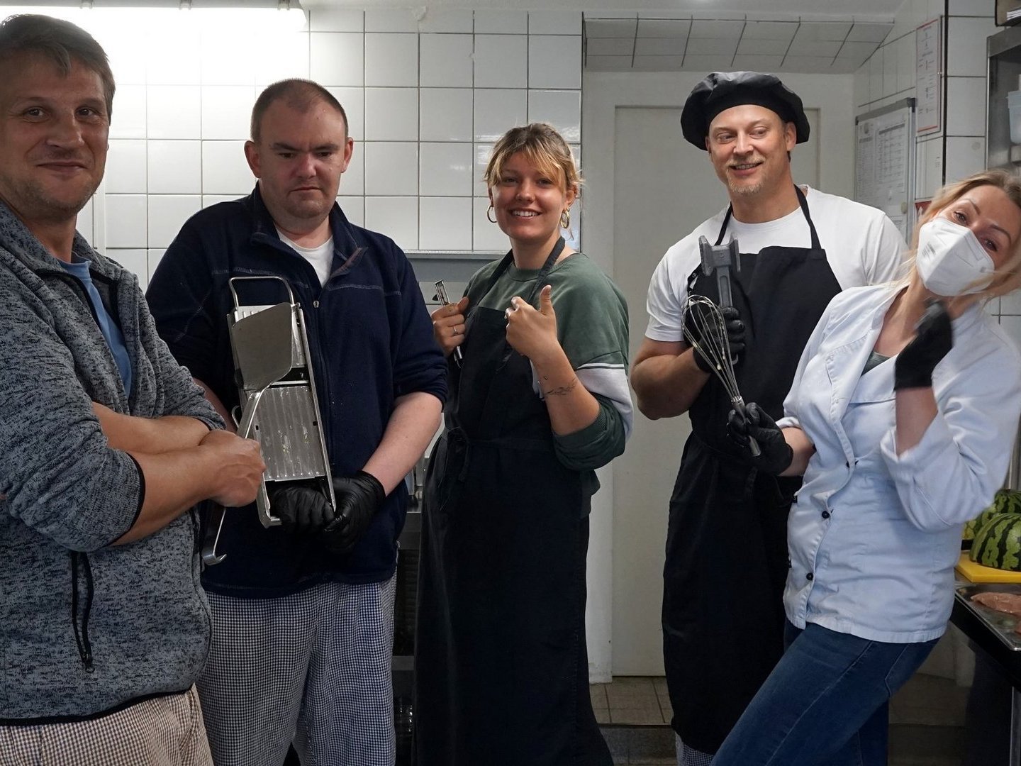 Küche: eine Gruppe Frauen und Männer in der Küche posen für ein Foto - jede/r mit einem Küchenwerkzeug in der Hand