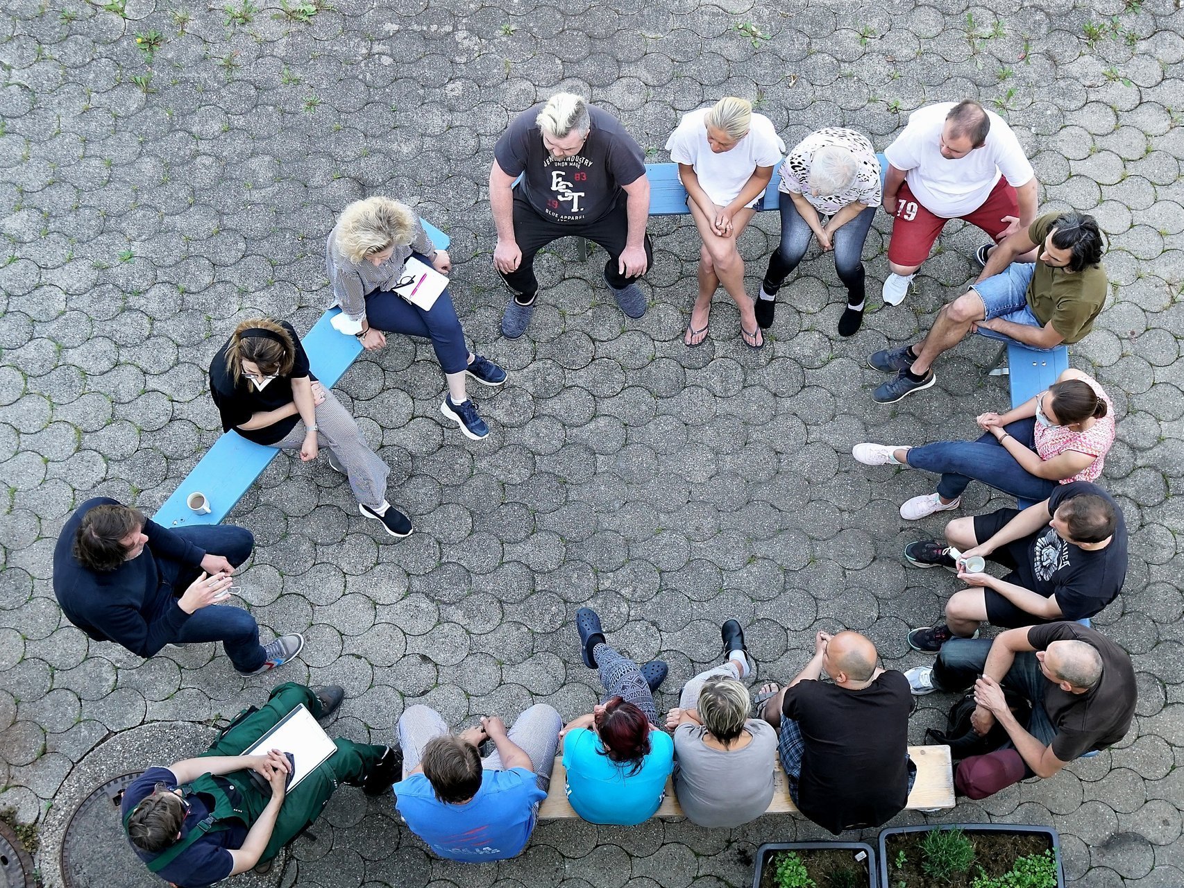 im Hof: eine Gruppe Frauen und Männer sitzen im Kreis auf Bierbänken und sprechen