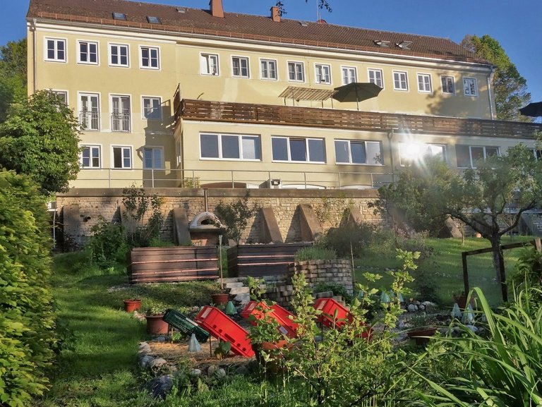 Aussenaufnahme: gelb gestrichenes Gebäude mit großer Terassen und einem Obst- und Kräutergarten
