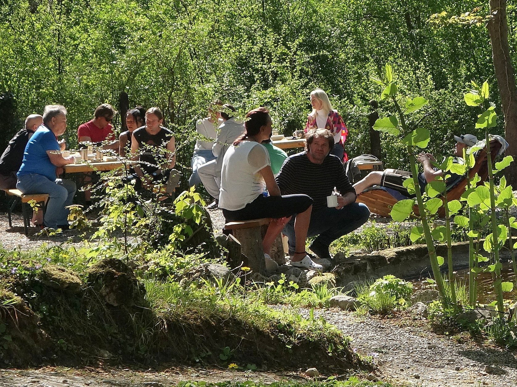 Chillen im Garten: Bewohner/innen sitzen auf Bänken und unterhalten sich oder liegen in Liegen 