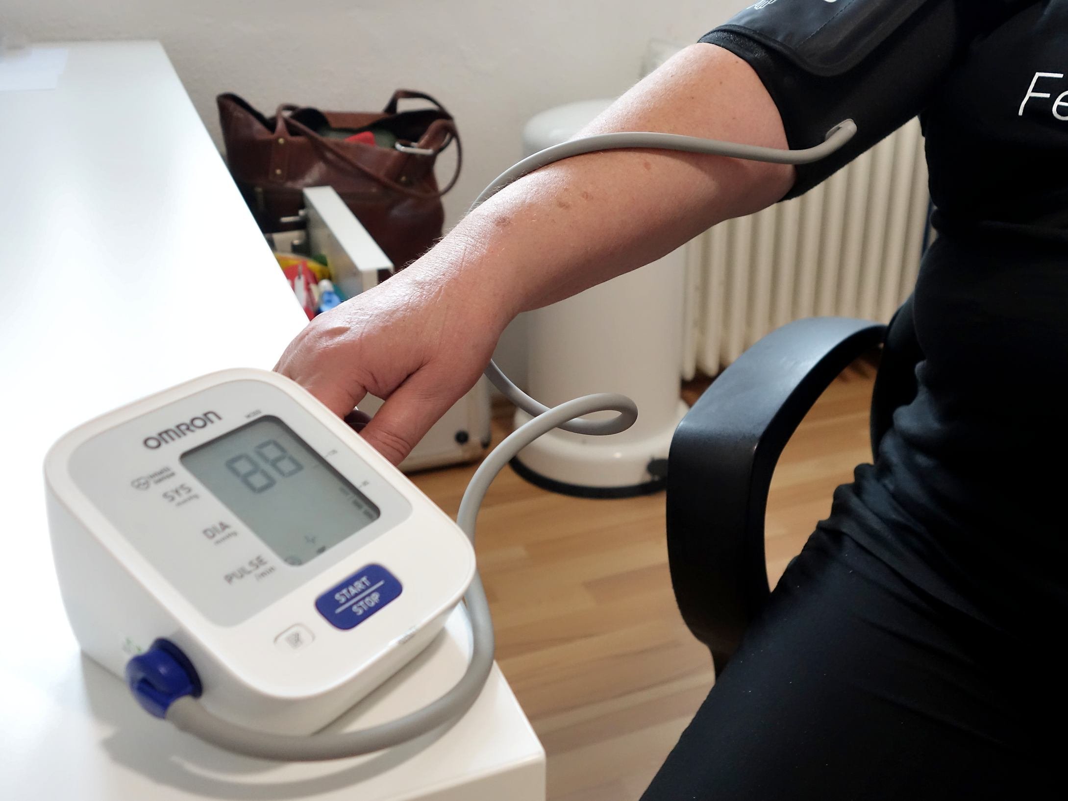 Elektronisches Blutdruck-Messgerät im Vordergrund - dahinter ein Arm mit Manschette