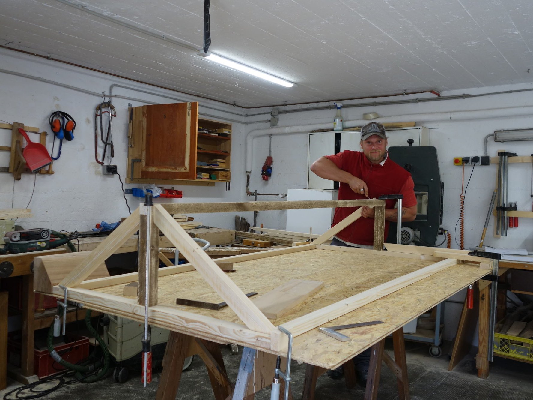 ein Mann in der Holzwerkstatt - er schraubt auf einer Arbeitsplatte ein Gestell zusammen
