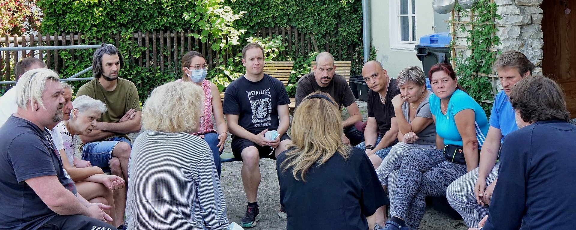 Terasse: eine Gruppe Frauen und Männer im Kreis auf Bierbänken im Gespräch